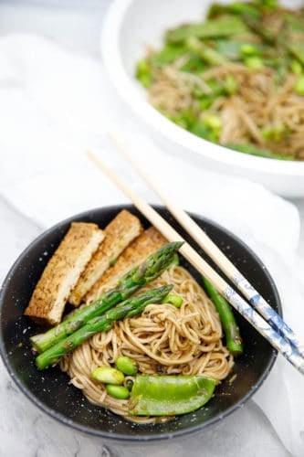 Overhead shot of soba noodle salad in black bowl on white background