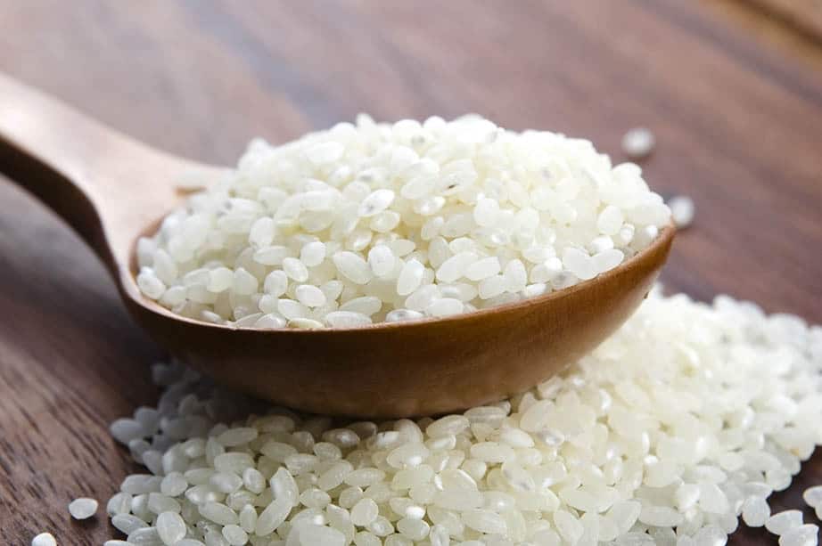 Raw sushi rice on a wooden spoon and dark background