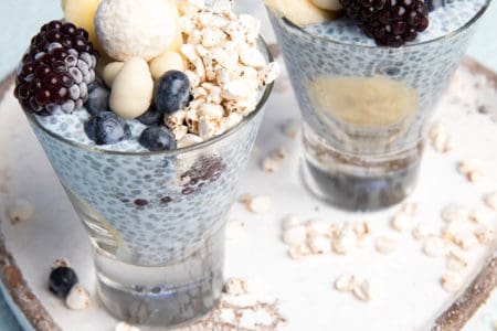 Layered blue chia puding in a glass with berries and banana