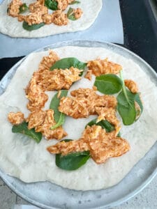 Adding ingredients to the pizza base, chicken , spinach and Buffalo sauce