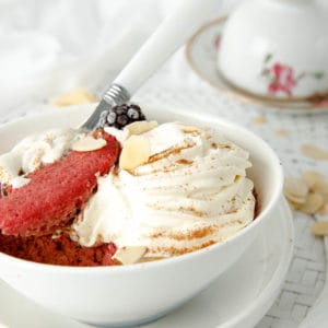 Red velvet keto mug cake in a white bowl with cream