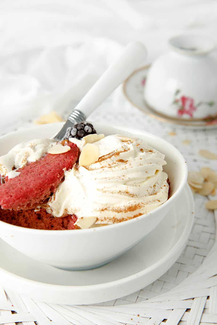 Red velvet keto mug cake in a white bowl with cream