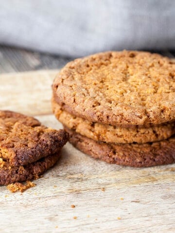 ANZAC biscuits stacked on a white background with a jug of milk