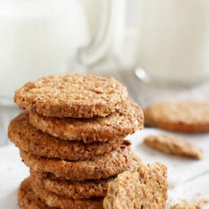 ANZAC biscuits stacked on a white background with a jug of milk