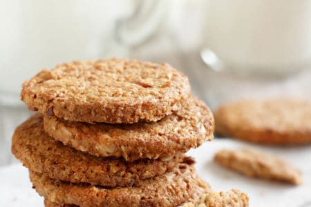 ANZAC biscuits stacked on a white background with a jug of milk