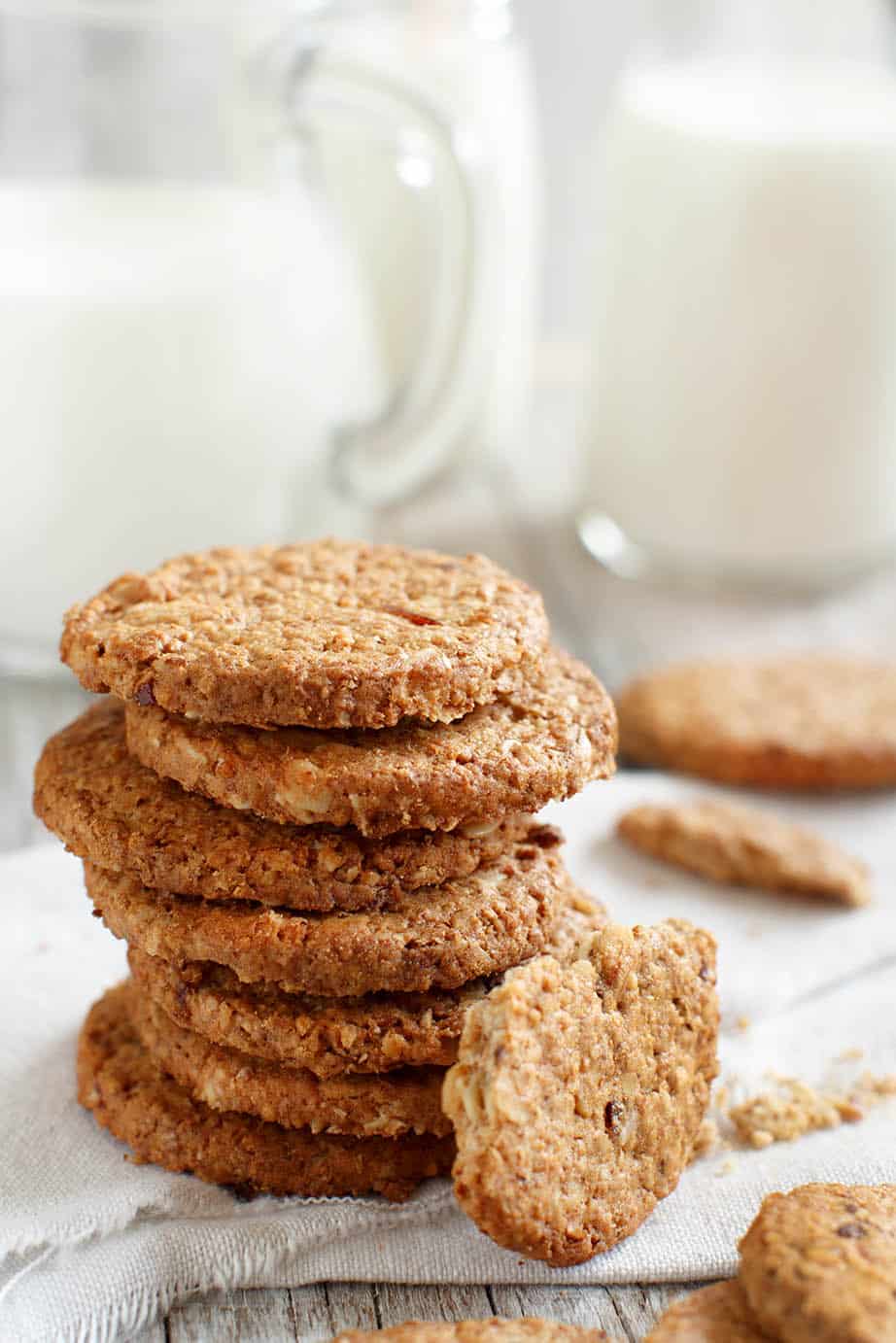 ANZAC biscuits stacked on a white background with a jug of milk