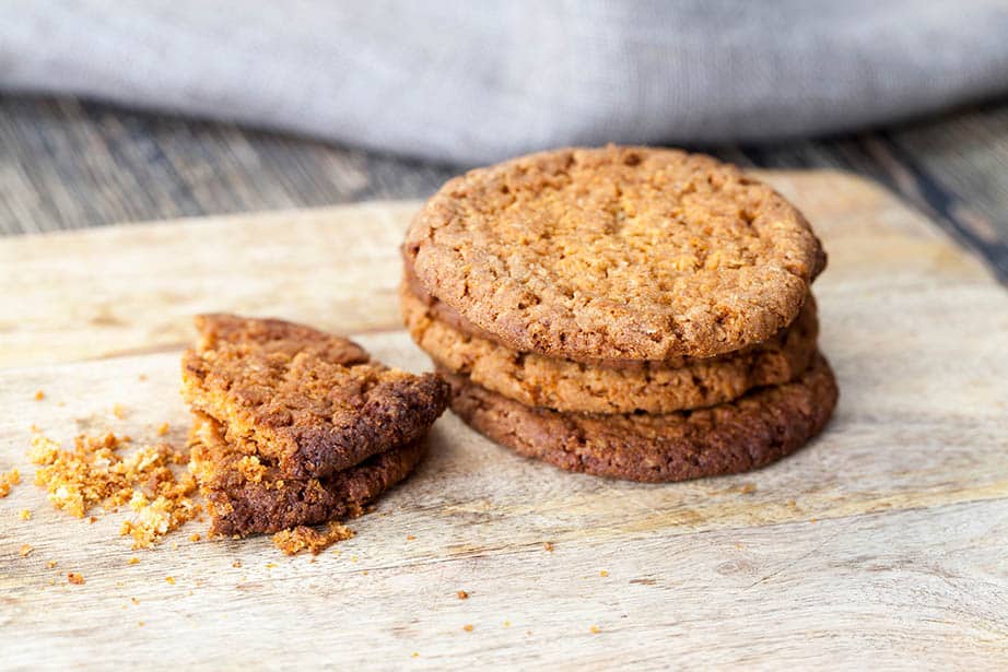 Anzac cookies stacked on a wooden bench one with a bite