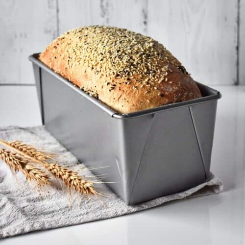 Seeded loaf of bread in a bread tin on the bench