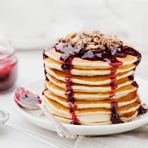 Square image of a close up stack of pancakes with dripping raspberry sauce