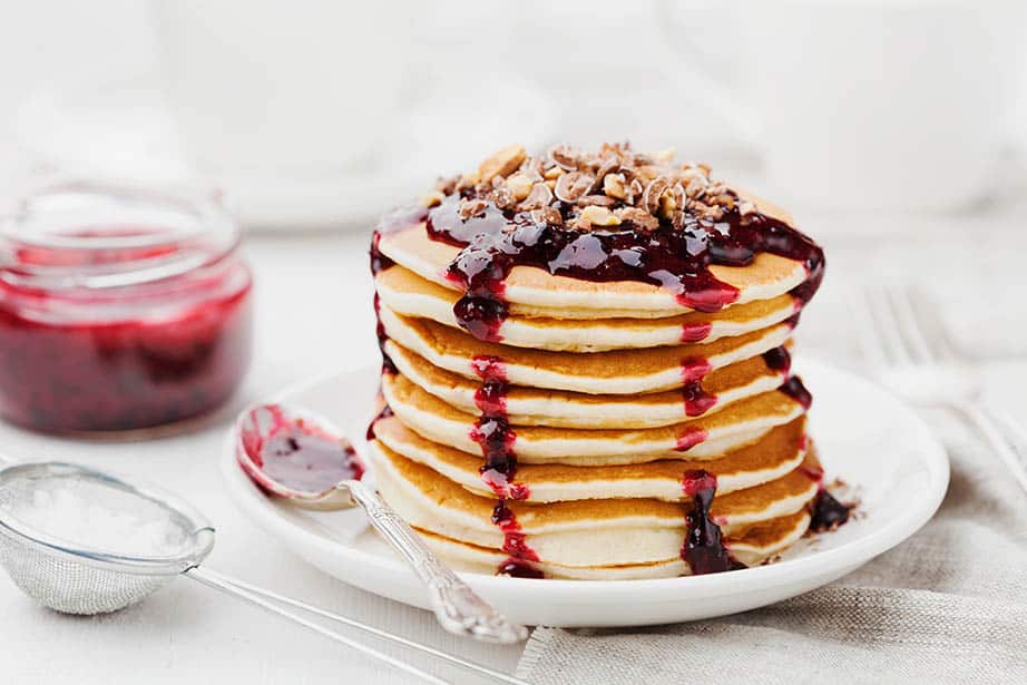 Table setting with a stack of pancakes with dripping red berry sauce