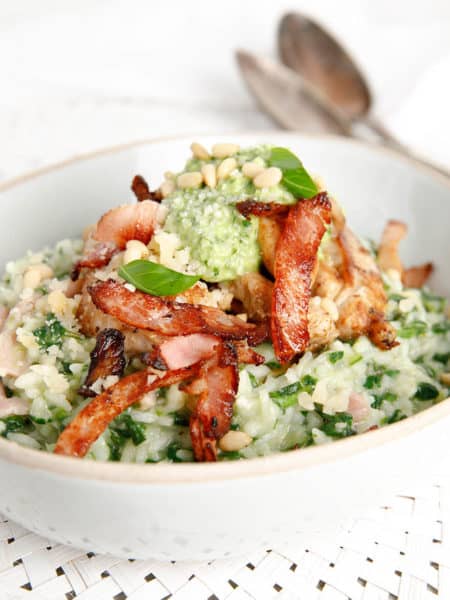 A bowl of chicken risotto topped with pesto and bacon on white background