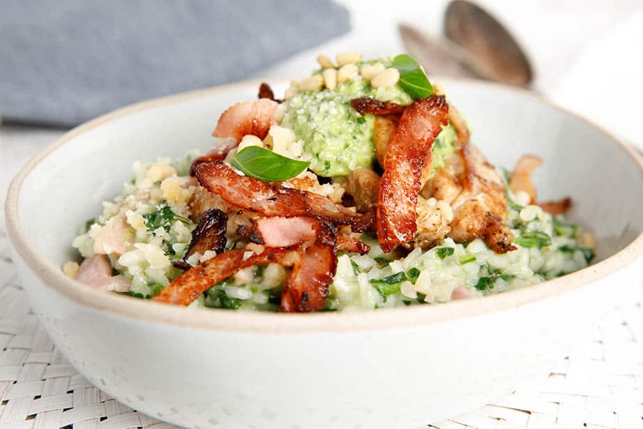 Close up chicken pesto risotto with bacon and pesto topping on white background