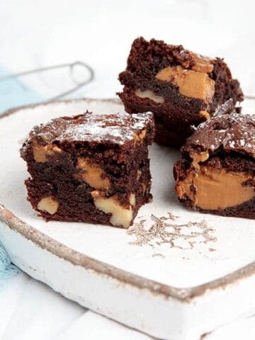 Landscape image of Caramel Chocolate Brownies on a plate and dusted with icing sugar