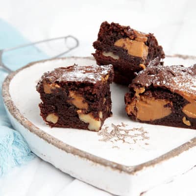 Landscape image of Caramel Chocolate Brownies on a plate and dusted with icing sugar