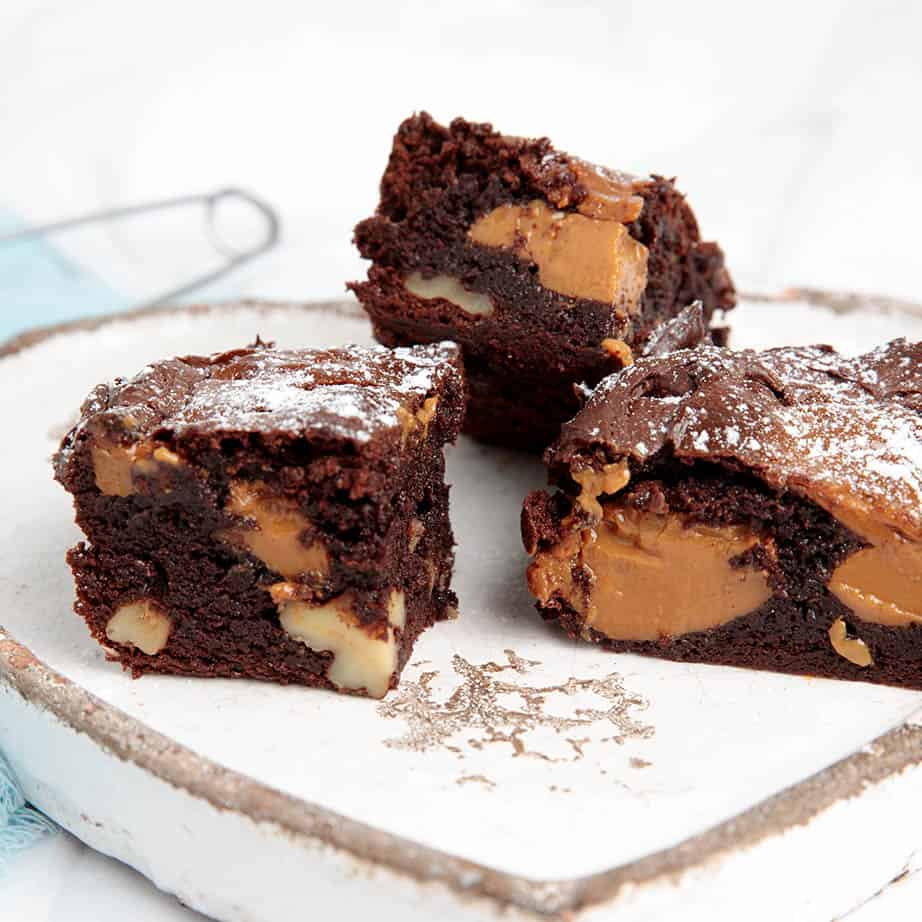 Square image of 3 slices of chocolate brownie on a white plate