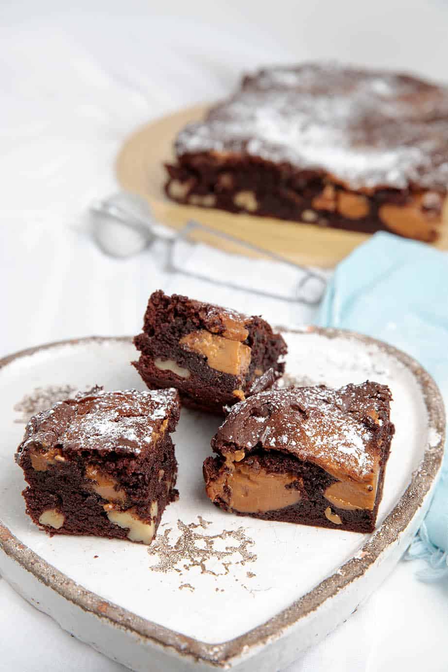 3 squares of Chocolate Caramel Brownie on a white platter with blue napkin