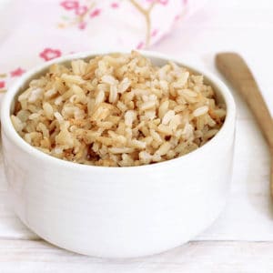 Cooked brown rice in a white bowl wooden spoon and floral serviette
