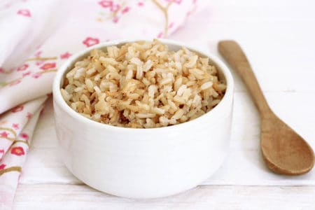 Cooked brown rice in a white bowl wooden spoon and floral serviette