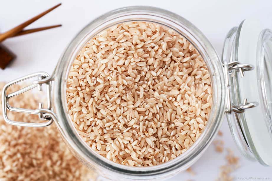 Raw brown rice in a glass jar on a white background
