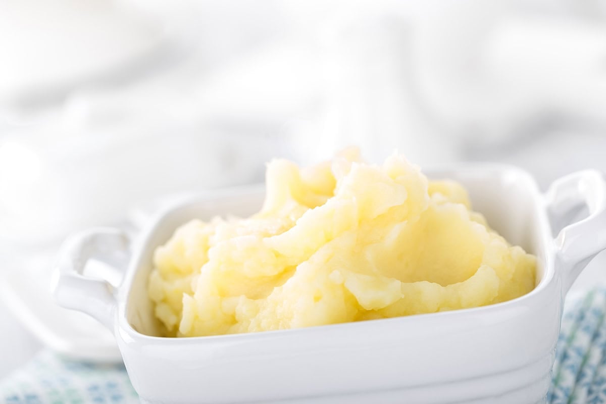 Portrail image fluffy Thermomix mash potato on a blue tea towel, white background