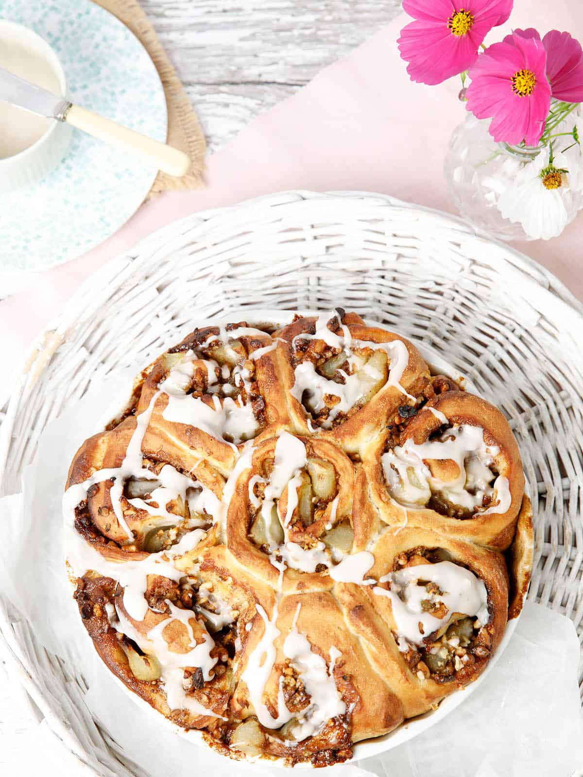 Cinnamon Scrolls dough made into Apple and walnut scrolls in a white baking dish with pink flowers in the background. These are like American Sticky Buns