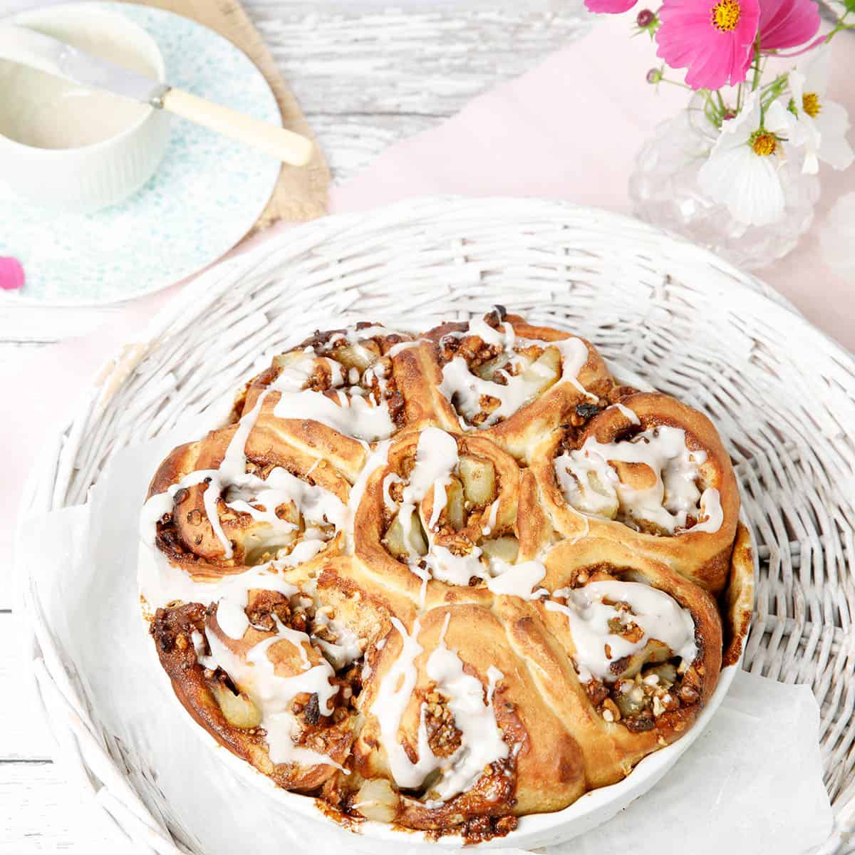 Cinnamon Scrolls dough made into Apple and walnut scrolls in a white baking dish with pink flowers in the background. These are like American Sticky Buns