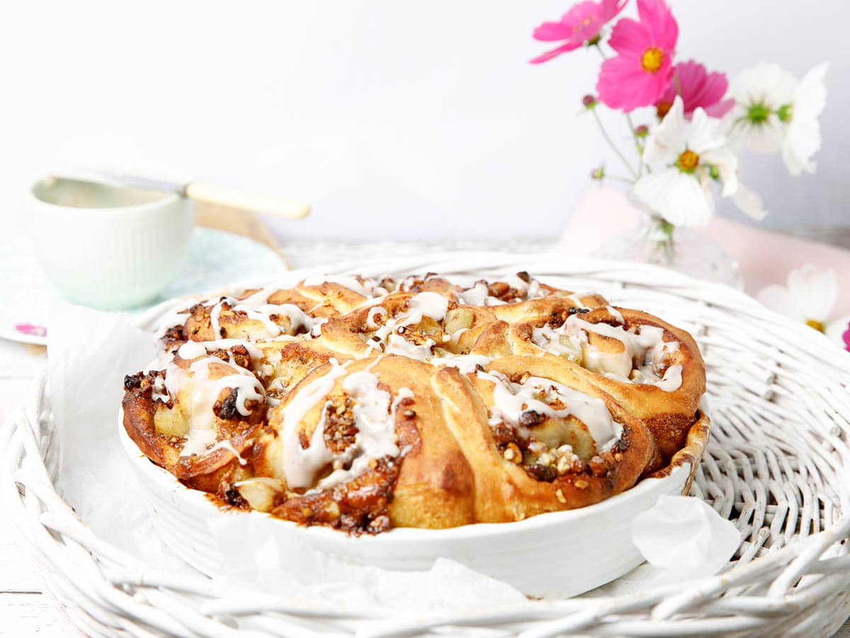 Cinnamon Scrolls dough made into Apple and walnut scrolls in a white baking dish with pink flowers in the background. These are like American Sticky Buns