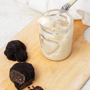 Truffle aioli in a jar with black truffles on a board