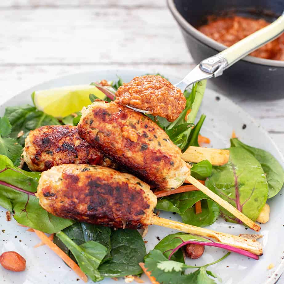 Peanut sauce being spooned over Chicken kebabs on a plate