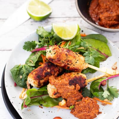 Sate Ayam Chicken Kebabs with salad greens and peanut sauce on a white plate