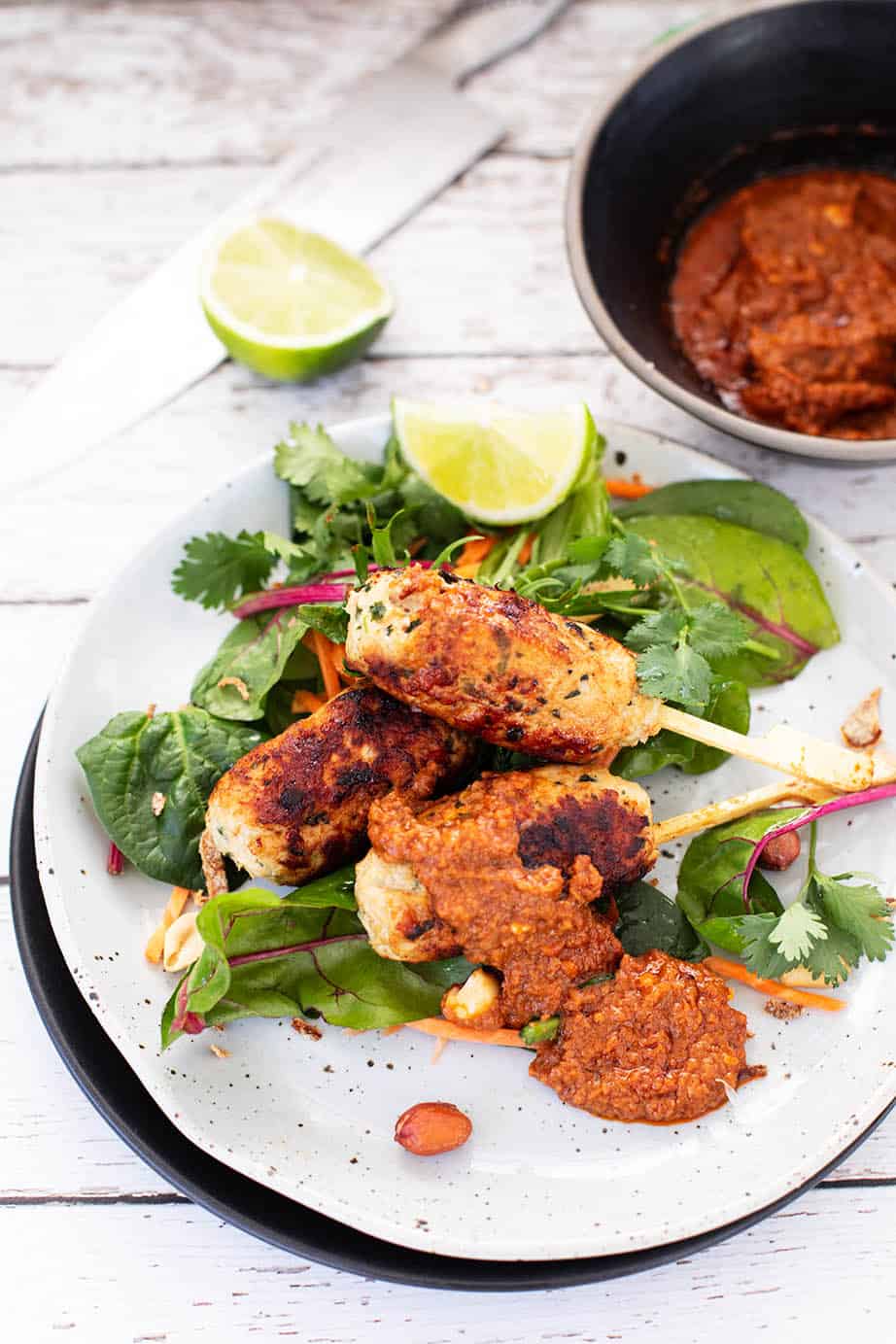 Sate Ayam Chicken Kebabs with salad greens and peanut sauce on a white plate