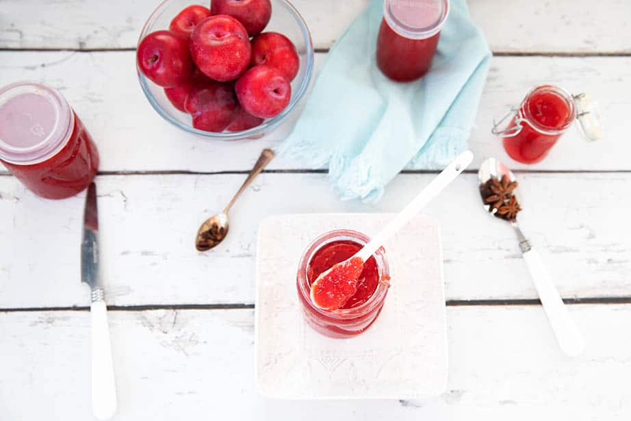 Overhead image of plum jam on a white teaspoon plums in the background