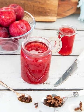 Plum jam on a white wooden background with spices in the foreground