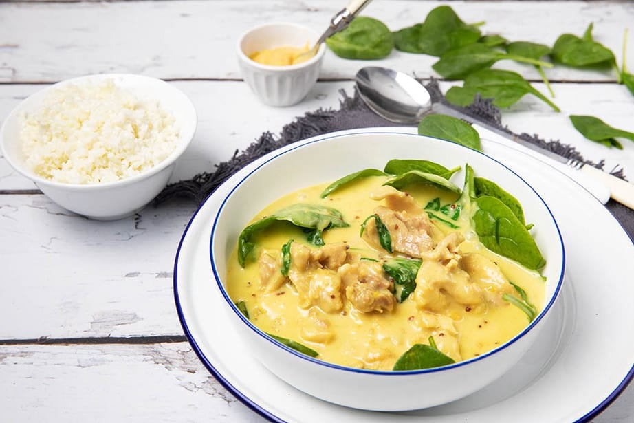 Honey mustard chicken in a bowl with baby spinach on a white wooden background