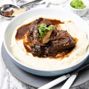 Large bowl of mashed potato covered in slow cooked beef cheeks on a cloth background