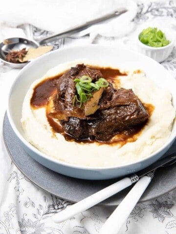 Large bowl of mashed potato covered in slow cooked beef cheeks on a cloth background