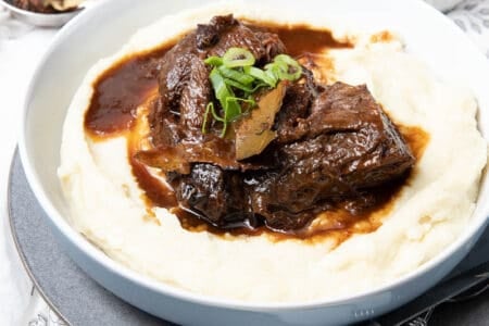 Large bowl of mashed potato covered in slow cooked beef cheeks on a cloth background
