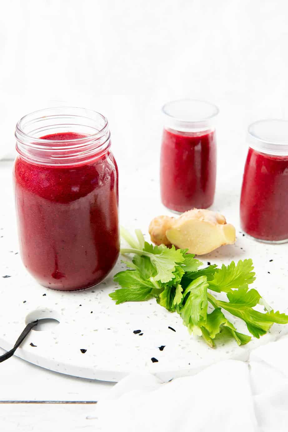 Berry Beetroot smoothie on a stone bench with ingredients like celery and ginger next to the smoothie