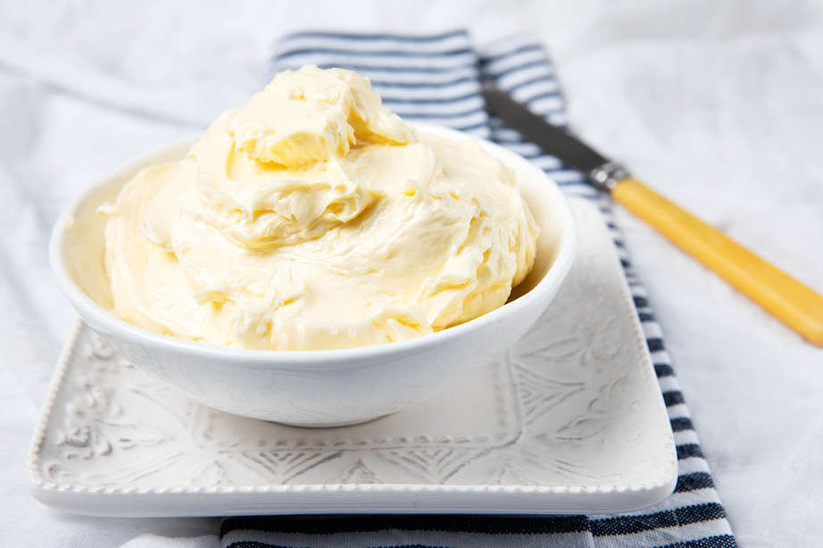 A bowl of homemade butter on white background with a striped napkin and old fashioned knife.