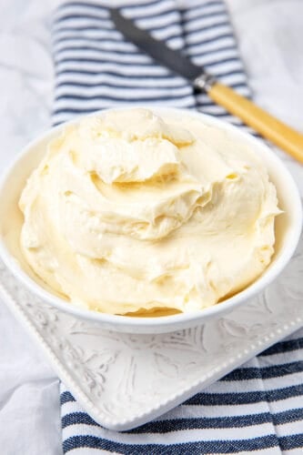 Homemade butter in a white bowl on a white background with a striped napkin