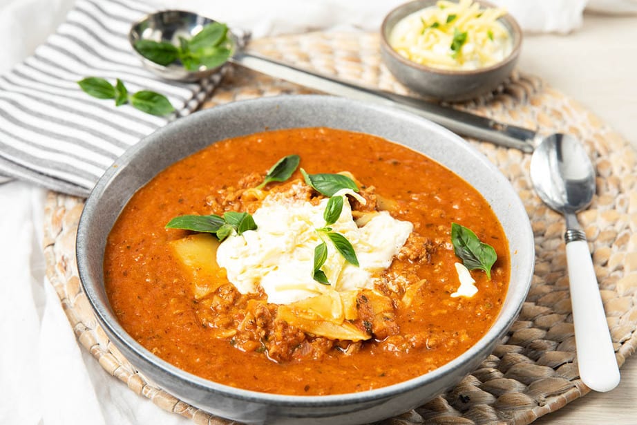 Landscape image of a bowl of Lasagna soup in a grey bowl. Placemat, napkins and cutlery in the picture.