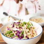 Apple coleslaw in a bowl and a hand adding slivered almonds