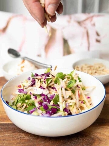 Apple coleslaw in a bowl and a hand adding slivered almonds