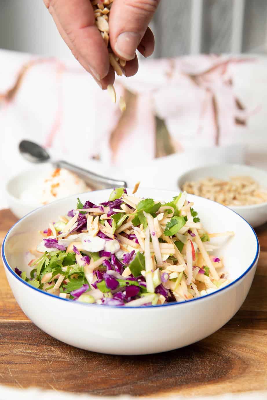 Thermomix coleslaw in a bowl and a hand adding slivered almonds