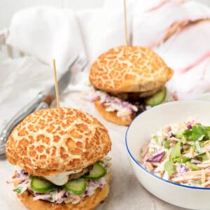 Two pork burgers on a white background with a bowl of slaw.