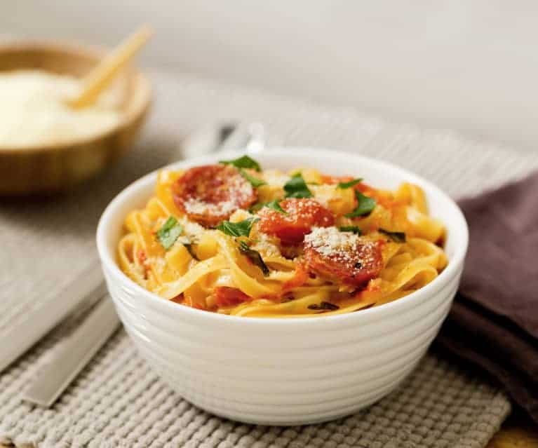 Creamy salami pasta in a white bowl and place mat