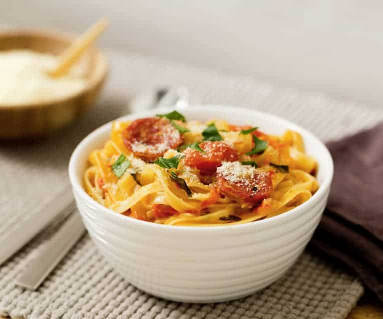 Creamy salami pasta in a white bowl and place mat