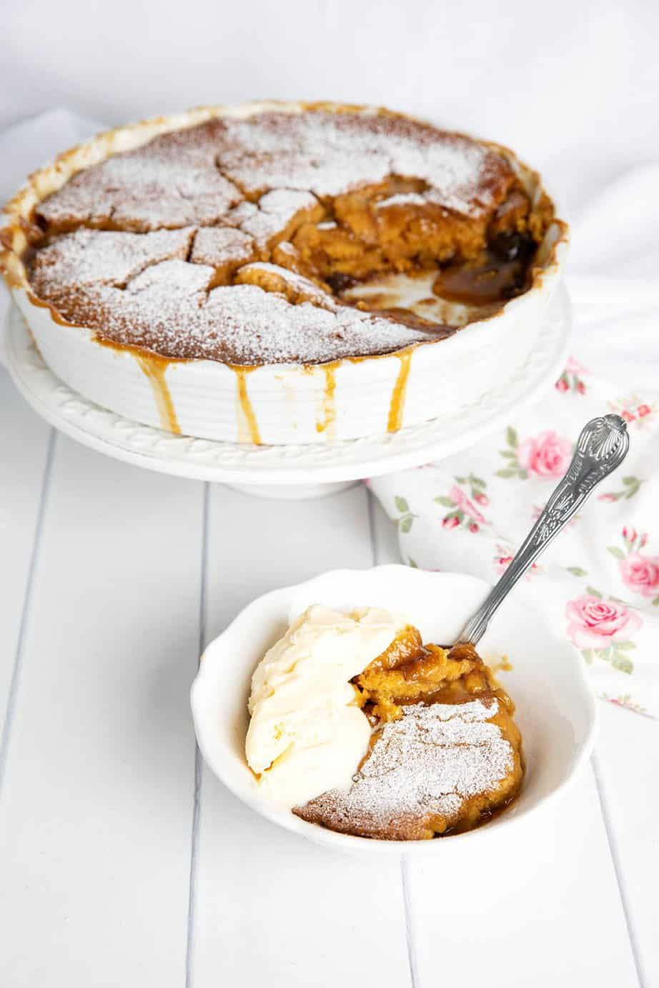 Portrait image of a bowl of butterscotch self saucing pudding Thermomix with ice cream and a dish of the pudding behind it.