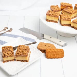 Biscoff Caramel slice on a white serving plate with knife and platter