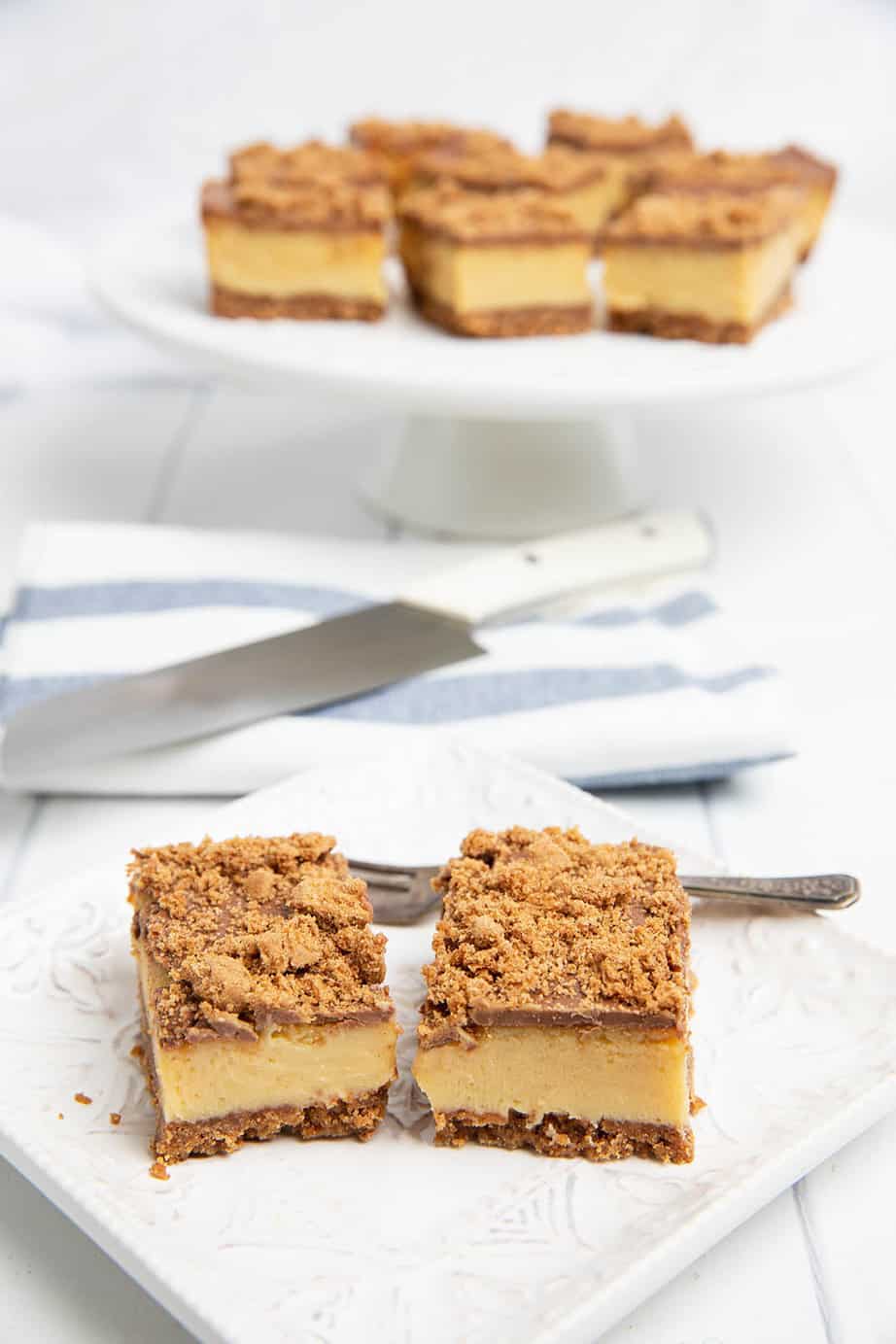 Biscoff Caramel Slice cut in pieces, two on a serving place and the rest on a platter